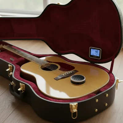An acoustic guitar stored in a hard case with an in-case humidifier and hygrometer